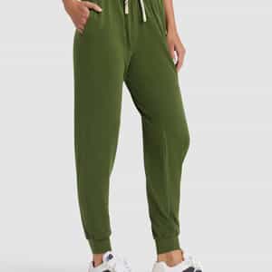 A person wears Cozy Earth's Women's Studio Jogger in olive green with a drawstring waist, paired with a white T-shirt and white sneakers, posing with one hand in their pocket against a plain background.|Color:Grove