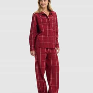 A woman stands barefoot, smiling, and wearing the Cozy Earth Women's Sutton Long Sleeve Pajama Set in red plaid—featuring a button-up top and loose pants—against a plain light background.|Color:Garnet Windowpane