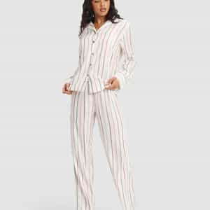 A woman wears the Cozy Earth Women's Soft Woven Long Sleeve Pajama Set, featuring white fabric with red and beige vertical stripes, a button-up collared top, and paired with maroon socks for a comfortable, relaxed look.|Color:Cottage Stripe