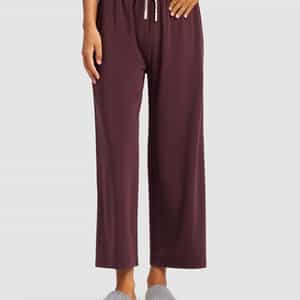 A person wearing Cozy Earth’s Women's Studio Cropped Wide Leg Pant in maroon, paired with a black top and gray slippers, stands against a plain light background.|Color:Raisin