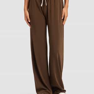 A person is standing against a light gray background wearing Cozy Earth's Women's Studio Wide Leg Pant in brown with white sneakers, hands relaxed by their sides. The pants feature a loose fit and drawstring waist.|Color:Espresso