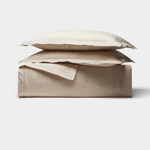 The Cozy Earth Soft-Wash Cotton Quilt Bundle features a neatly folded set of light beige bed sheets and two matching pillowcases, stacked on a plain surface against a white background.|Color:Driftwood