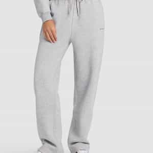 A woman models Cozy Earth's Women's Cityscape 2.0 Wide Leg Pant in light gray, paired with a matching sweatshirt and white sneakers with light brown soles. She stands against a plain white background, one hand in her pocket.|Color:Heather Grey