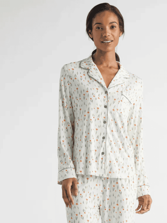 A person is wearing a matching pajama set with a pattern of small, colorful abstract shapes on a light background. They are standing and smiling with hands by their sides, against a plain, neutral backdrop.|Color:Sienna Tulips