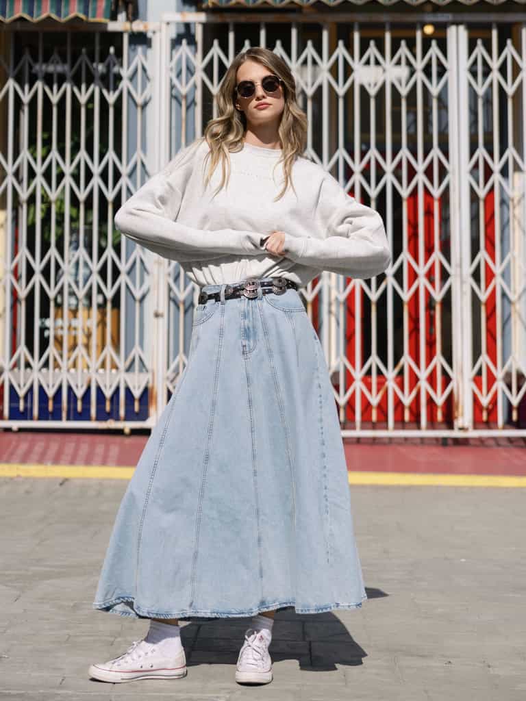 Heather Grey CityScape Pullover Crew. The Pullover is being worn by a female model. An accompanying jean skirt is being worn to complete the look of the outfit. The photo was taken with a downtown city background. |Color:Heather Grey