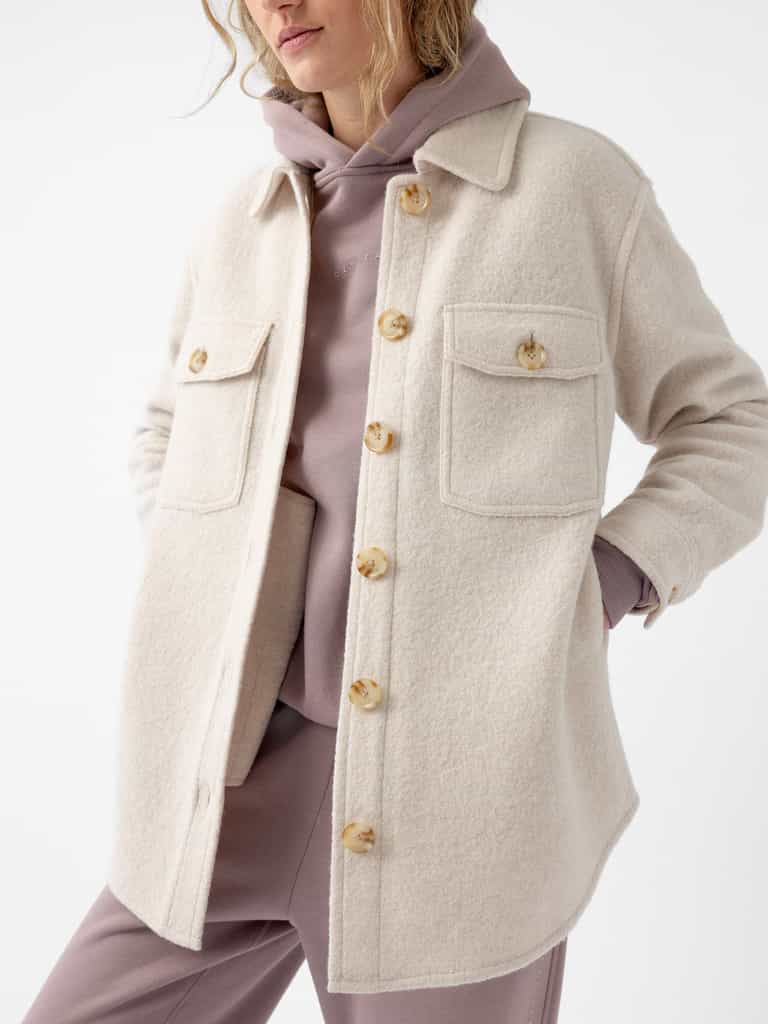 A person wearing a Cozy Earth Women's Boucle Shacket in beige over a mauve hoodie and matching pants. The shacket features large buttons and two front pockets, with their hands tucked into the pockets. The background is plain white. |Color:Alabaster