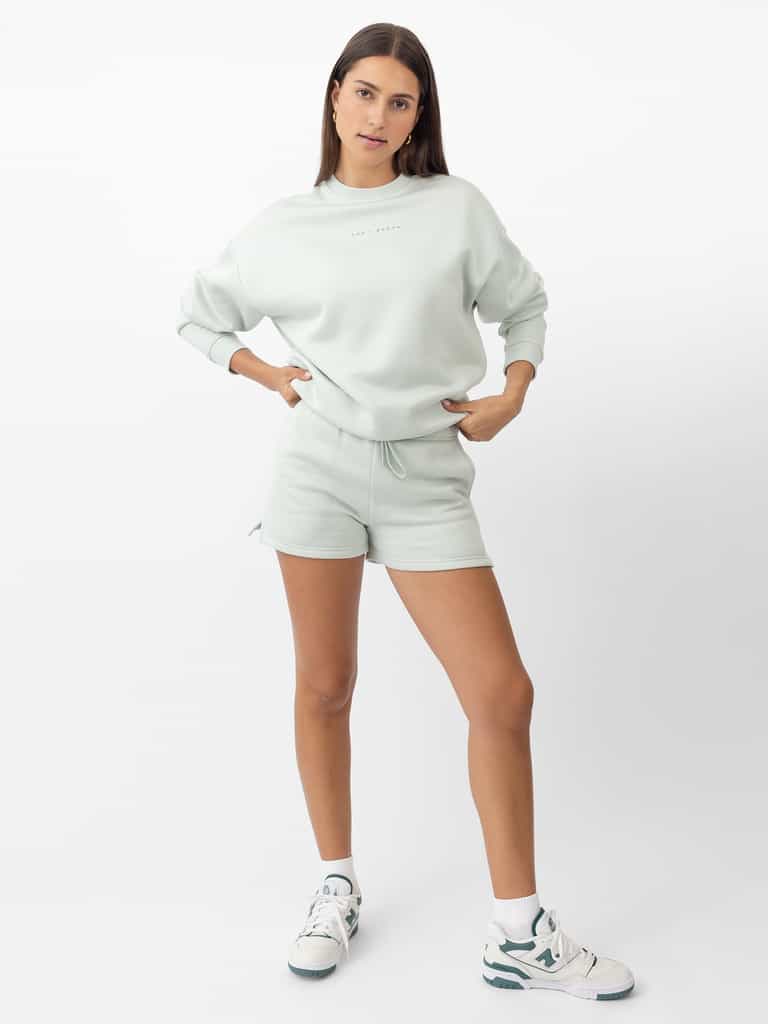 Arctic CityScape Pullover Crew. The Pullover is being worn by a female model. Accompanying city scape clothing is being worn to complete the look of the outfit. The photo was taken with a white background. |Color:Arctic