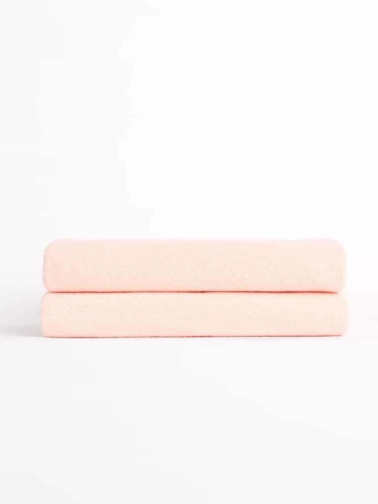 Two Luxe Bath Towels from Cozy Earth, neatly folded in light pink, stacked against a white background. |Color:Blossom