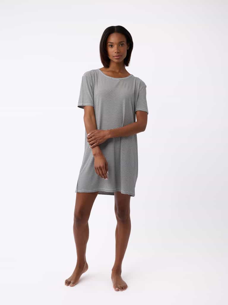 A person wears a Cozy Earth Women's Bamboo Stretch-Knit Sleep Dress, light gray and knee-length, standing barefoot against a plain white background with arms gently crossed. The short-sleeve dress offers a relaxed and comfortable fit. |Color:Eclipse Mini Stripe