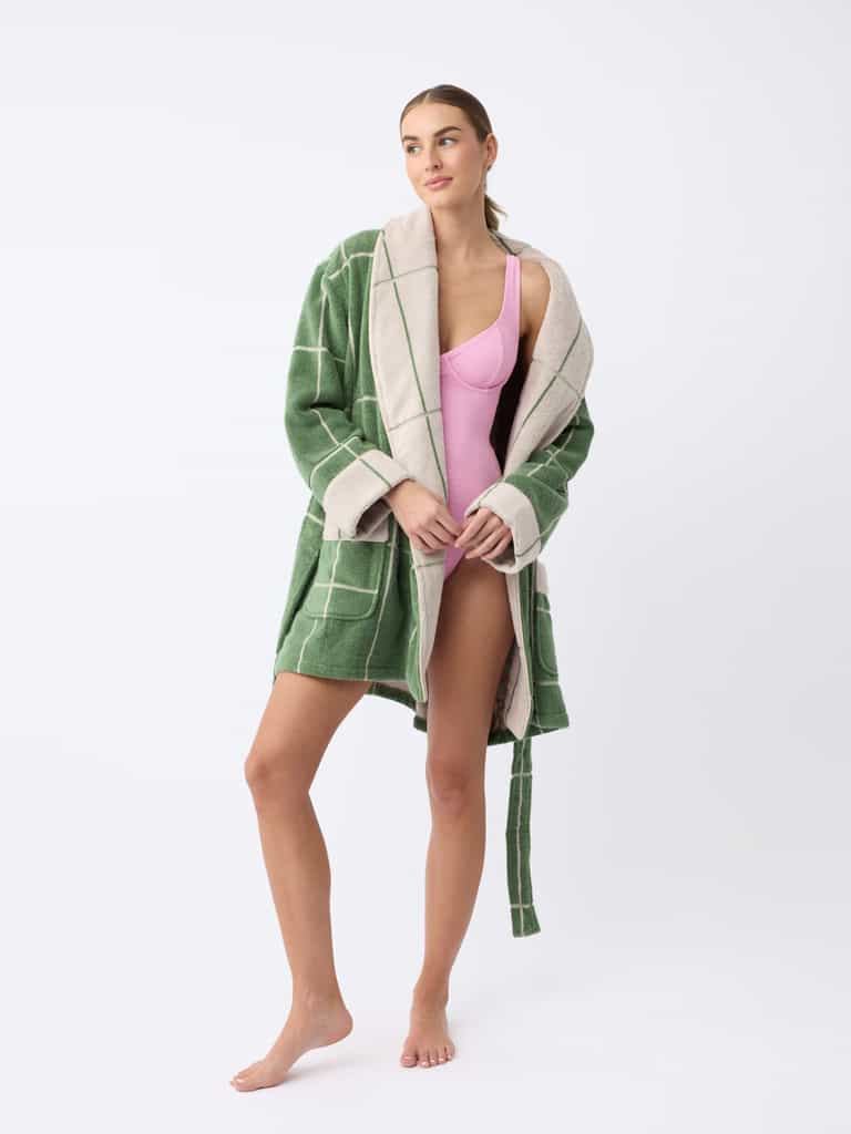 A person stands barefoot against a plain white background, wearing Cozy Earth's Windowpane Resort Robe in green and white checkers over a pink swimsuit. They have long hair and maintain a relaxed sideward gaze. |Color:Prickly Pear