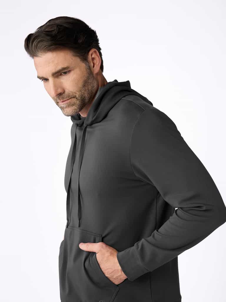A man with dark hair and a beard wears the Cozy Earth Men's Brushed Bamboo Hoodie & Jogger Set in dark gray, standing with one hand in his pocket and looking slightly downward against a plain white background. |Color:Charcoal