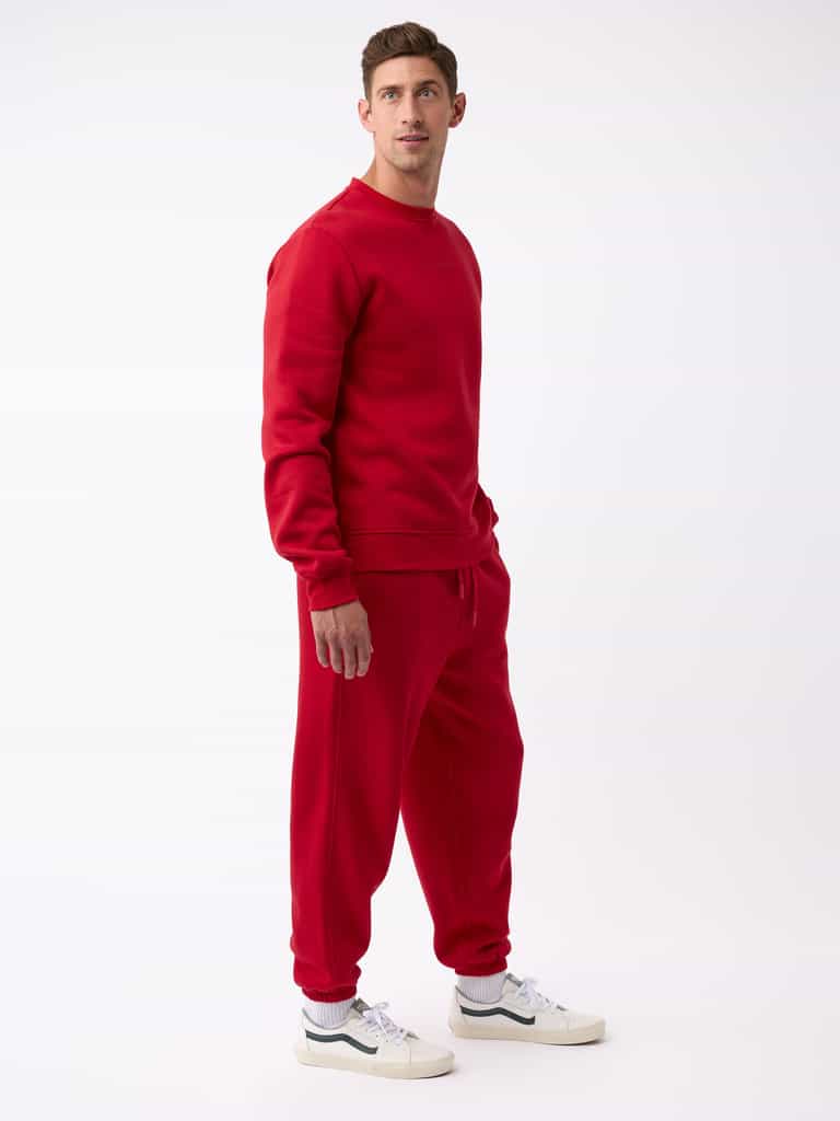 A person wearing the Men's CityScape Sweatpant by Cozy Earth along with a matching red sweatshirt stands against a plain white background. They are gazing slightly to the right and have white sneakers on. |Color:Crimson