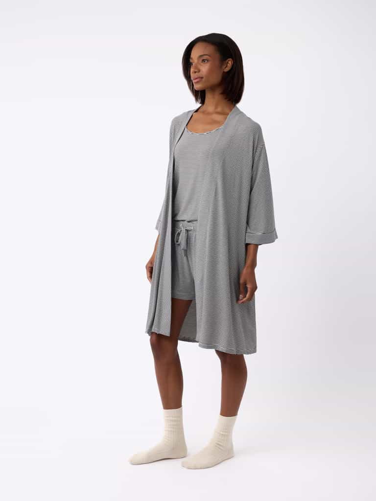 Clad in a Cozy Earth Women's Bamboo Stretch-Knit Kimono Robe over matching shorts and tank top, a person with short dark hair sports cream-colored socks against a plain white backdrop. |Color:Eclipse Mini Stripe