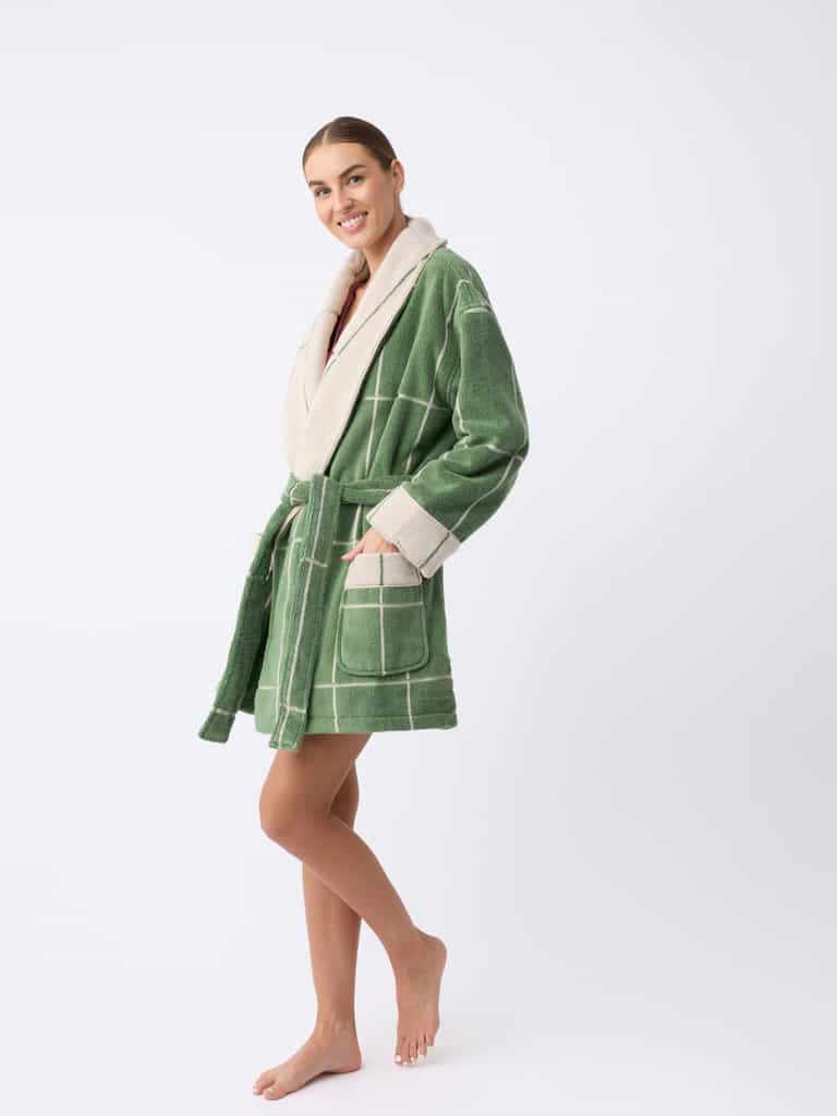 A smiling person stands barefoot in a Windowpane Resort Robe by Cozy Earth, featuring a green and white checkered pattern with cream-colored trim, posing against a plain white background. |Color:Prickly Pear