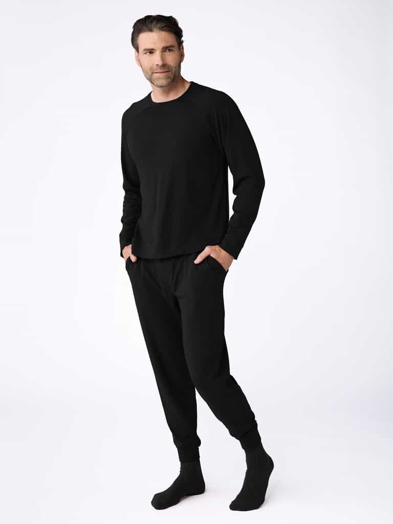 A man dons the Cozy Earth Men's Bamboo Jogger Set, with hands in pockets, pairing it perfectly with black socks against a plain white wall. |Color:Black