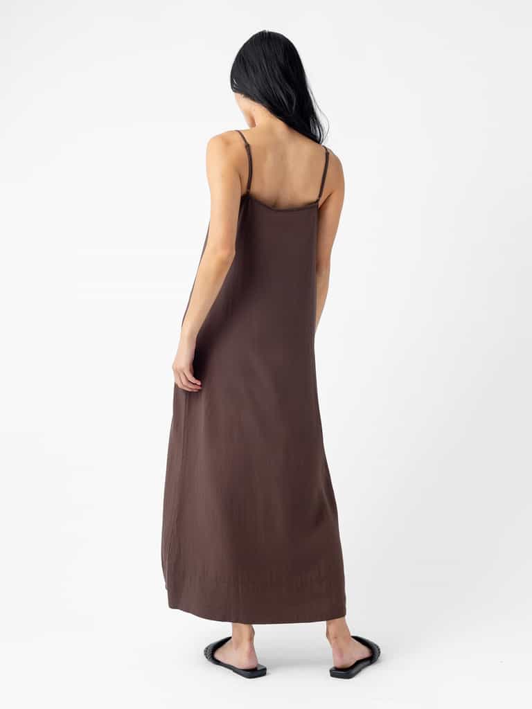 A woman with long dark hair is standing with her back to the camera, wearing a Cozy Earth Women's Sunset Slip Dress and black sandals. The background is plain white. |Color:Cacao
