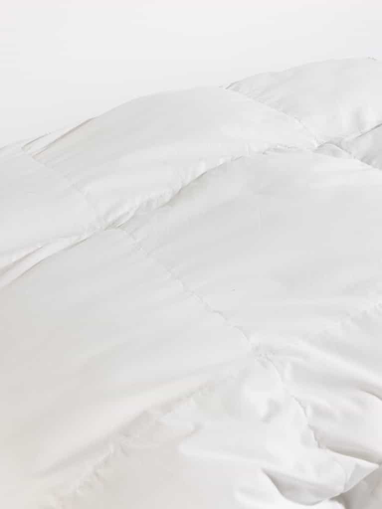 Close-up of a white, quilted fabric with visible stitching, creating a checkerboard pattern. The material appears soft and plush, suggesting it is part of the Cozy Earth's Down Alternative Comforter.|Filling:Standard