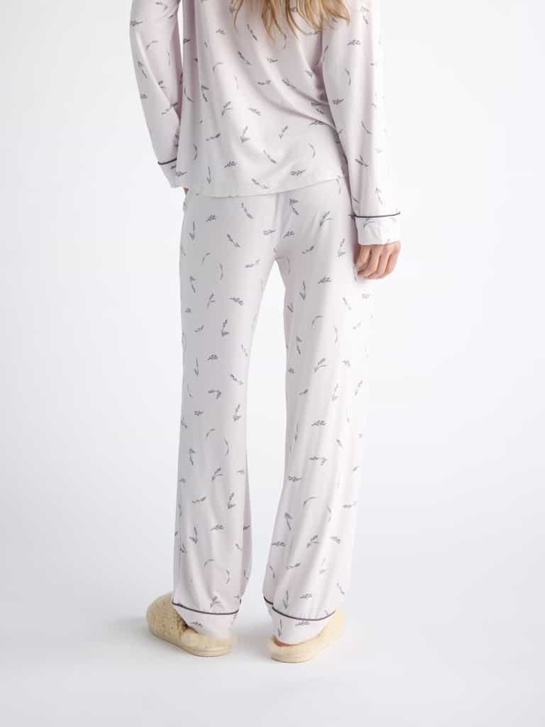 Back view of someone wearing Cozy Earth Women's Bamboo Stretch-Knit Pajama Pant in a light color with a subtle pattern, paired with fluffy slippers. The person has long hair and stands against a plain white background. |Color:French Lavender