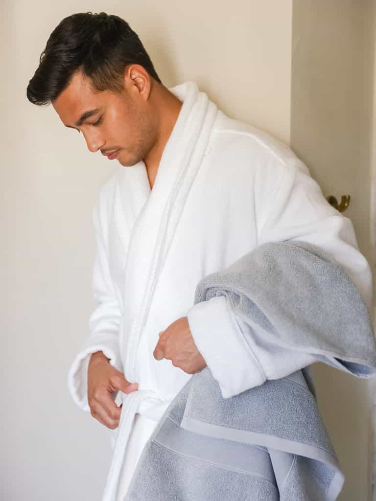 Man in white robe holding harbor mist luxe bath towel |Color:Harbor Mist