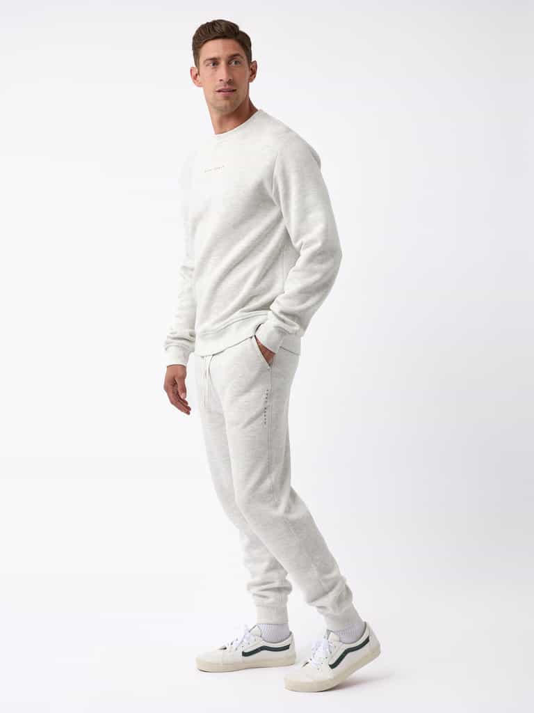 A person stands against a white background, dressed in the Men's CityScape Jogger by Cozy Earth, paired with white sneakers. The outfit exudes a casual and comfortable vibe. |Color:Heather Grey