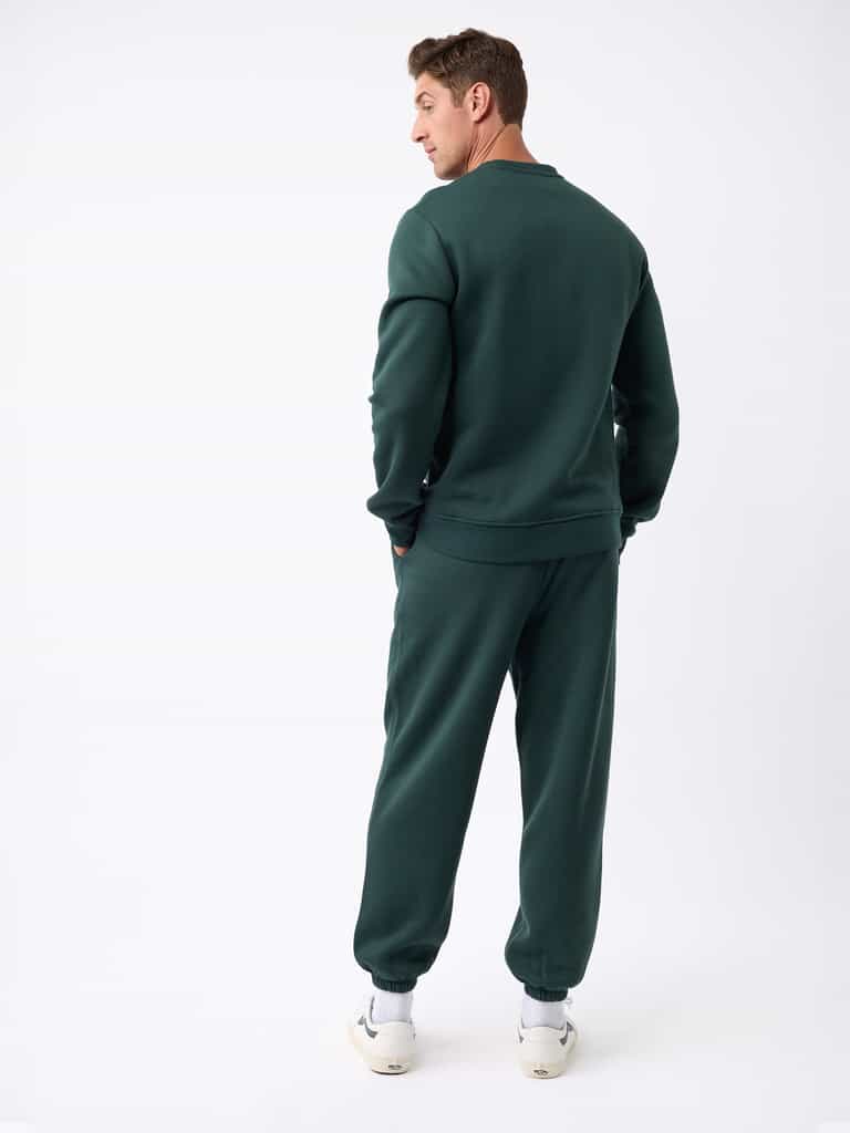 A person wearing the Cozy Earth Men's CityScape Sweatpant and white sneakers stands facing away, looking over their shoulder against a plain white background, which highlights the clothing. |Color:Spruce