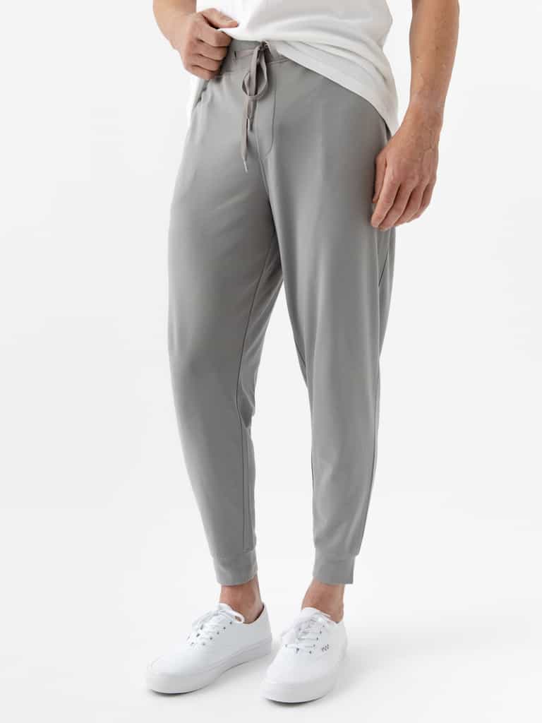 A person wearing Cozy Earth's Men's Bamboo Jogger Set in light gray, complemented by a white T-shirt and sneakers, against a plain white background. |Color:Stone