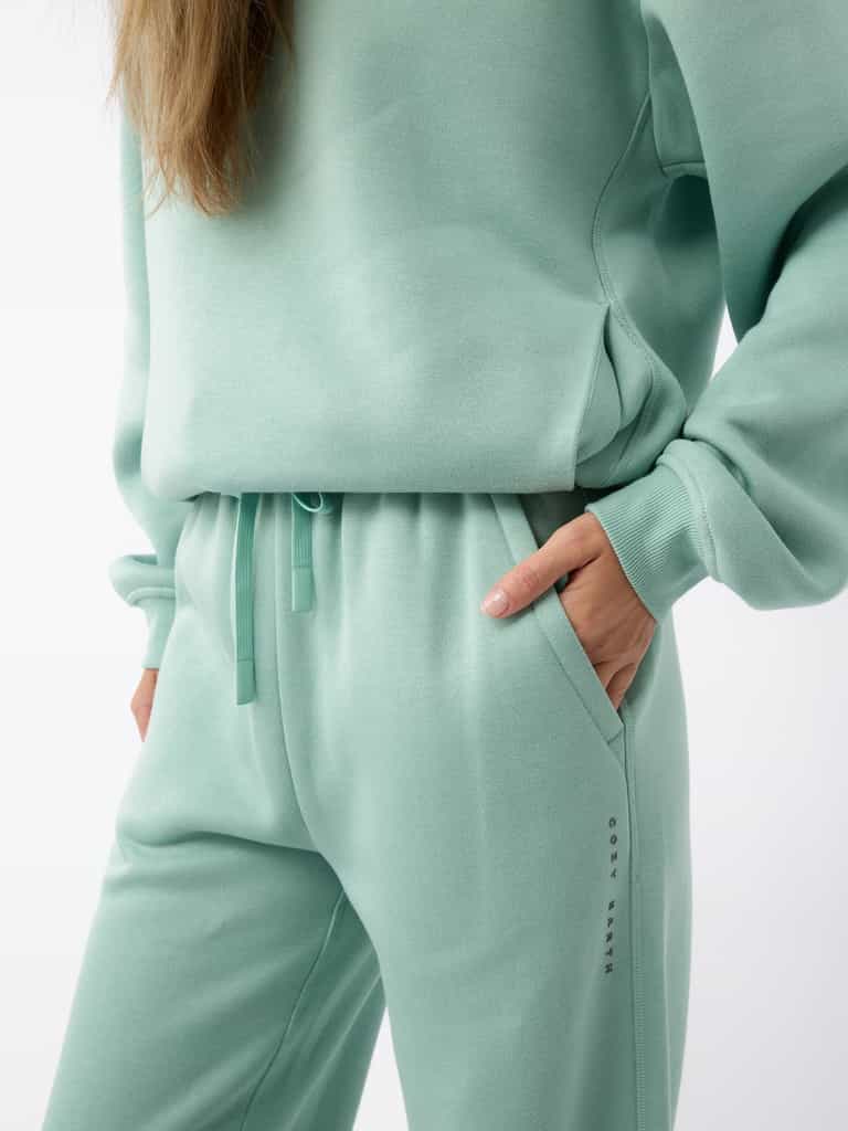 Close-up of a person wearing a mint green tracksuit from Cozy Earth with one hand in their pocket. The ensemble features the Women's CityScape Wide Leg Pant and a coordinating sweatshirt. The fabric appears soft and comfortable. |Color:Wintergreen