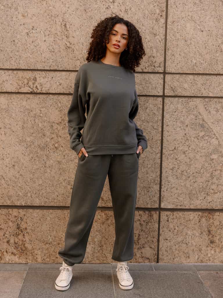 Storm CityScape Pullover Crew. The Pullover is being worn by a female model. Accompanying city scape clothing is being worn to complete the look of the outfit. The photo was taken with a city building background. |Color:Storm