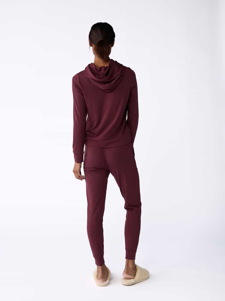 A person stands facing away, wearing Cozy Earth's Women's Bamboo Jogger Pant in maroon and beige slippers. The plain white background accentuates the outfit. |Color:Burgundy