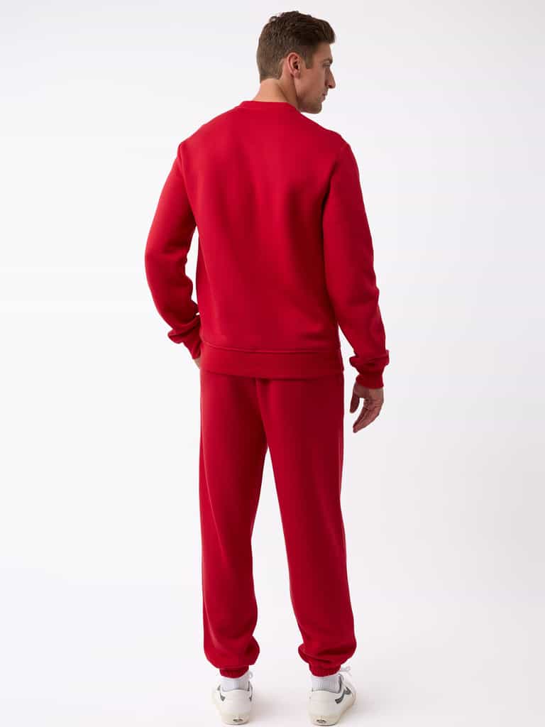 A person stands facing away, donning a matching red Men's CityScape Crewneck from Cozy Earth paired with white sneakers. The plain white background accentuates the vibrant color of the outfit. |Color:Crimson
