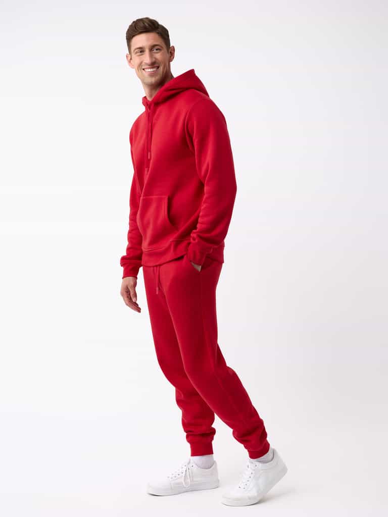 A person stands smiling, dressed in a matching Cozy Earth red hoodie and Men's CityScape Jogger, complemented by white sneakers against a plain white background. |Color:Crimson