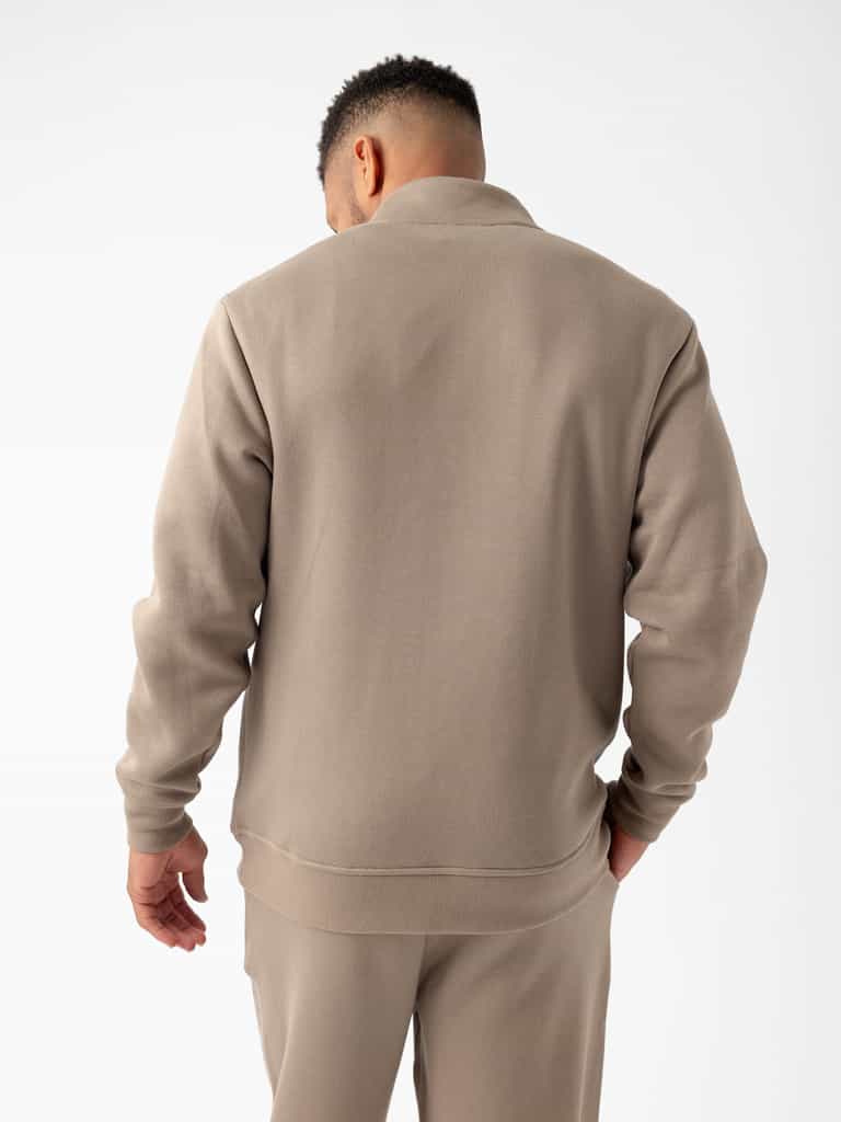 A person with short, curly hair is standing with their back facing the camera, wearing a light brown Cozy Earth Men's CityScape Quarter Zip fleece sweater and matching pants. The background is plain white. |Color:Ebony