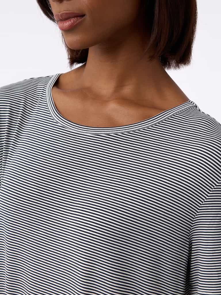 A close-up shows a person in the Women's Bamboo Stretch-Knit Sleep Dress by Cozy Earth. The black and white striped dress features a round neckline. A plain, light-colored background highlights the textured fabric and design. |Color:Eclipse Mini Stripe