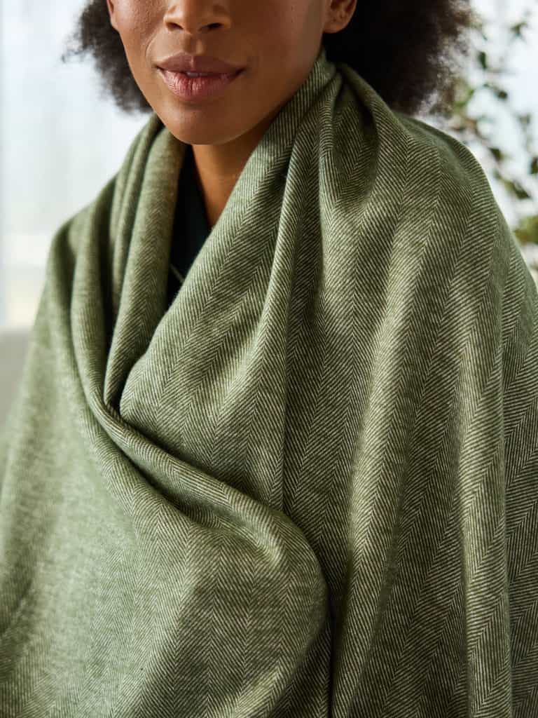 Close up of woman with ivy herringbone tassel throw wrapped around her |Color:Ivy