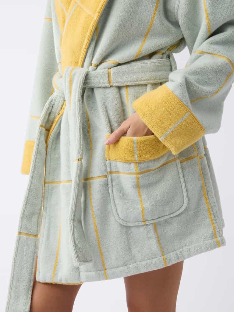 A person in a Cozy Earth Windowpane Resort Robe, showcasing a yellow and green checkered pattern with large pockets and a matching belt, stands with one hand in a pocket against a plain white background. |Color:Sunny Sky