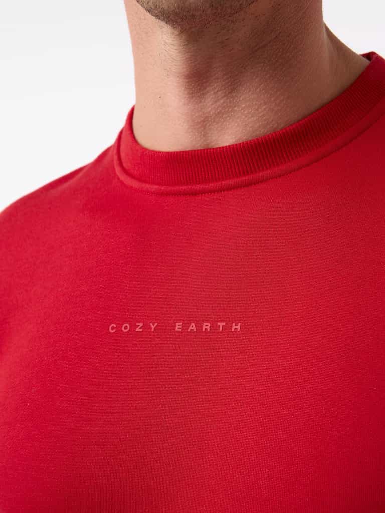 Close-up of a person wearing the Men's CityScape Crewneck in red, featuring the brand name "Cozy Earth" printed in small white letters. The focus is on the textured fabric and subtle design. |Color:Crimson