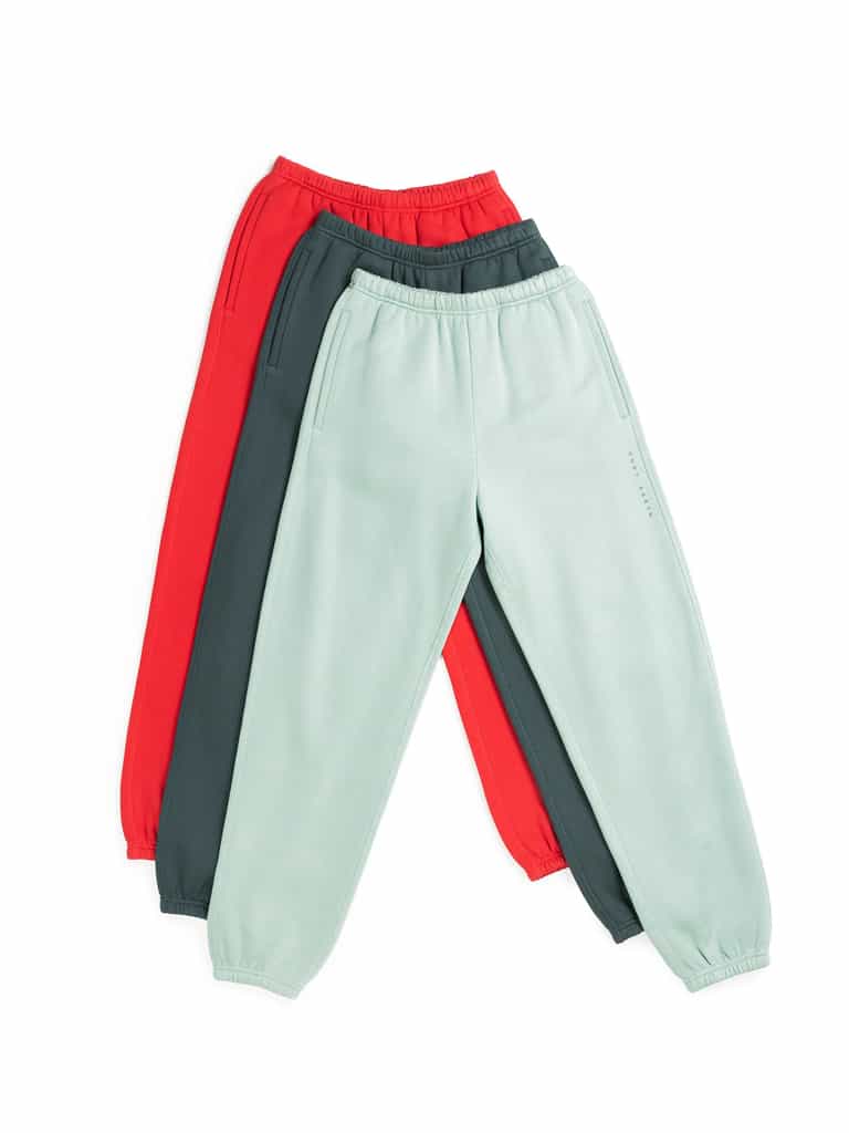 Three pairs of Men's CityScape Sweatpants from Cozy Earth in red, dark green, and light green are laid flat, stacked together. Each features an elastic waistband and cuffs, with subtle pocket details. |Color:Crimson
