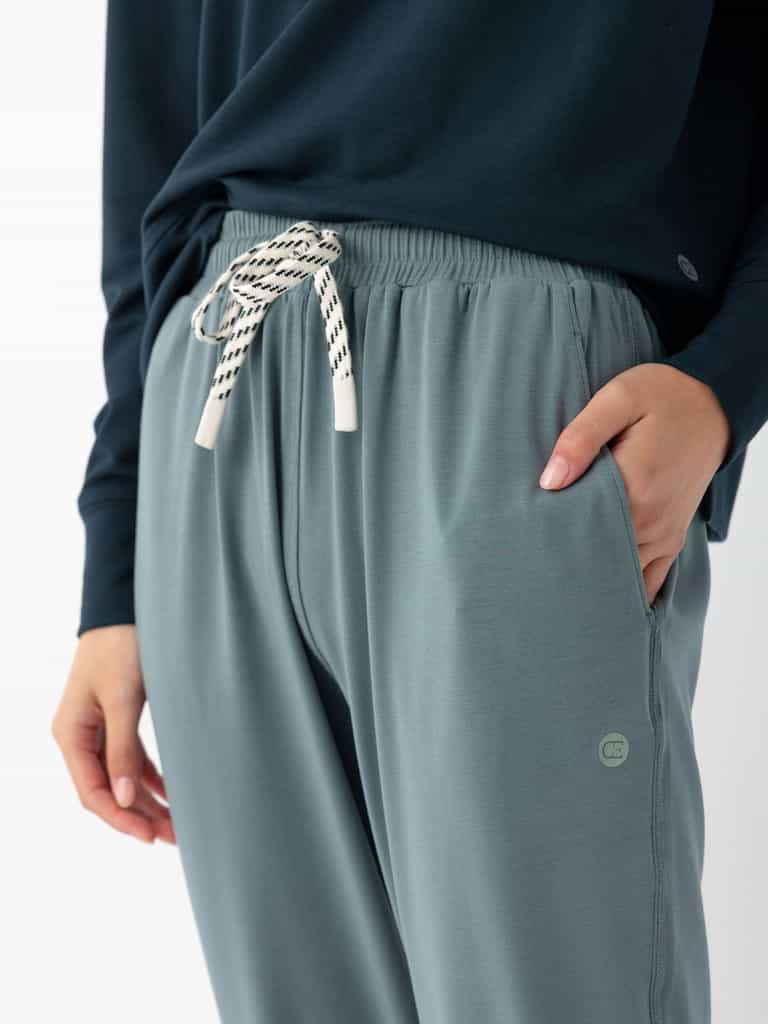 Close-up of a person wearing Cozy Earth's Women's Studio Jogger in light blue-gray with white drawstrings, paired with a dark blue long-sleeve top. The person's right hand is in the pocket, showcasing the joggers' casual and comfortable style. |Color:Deep Blue