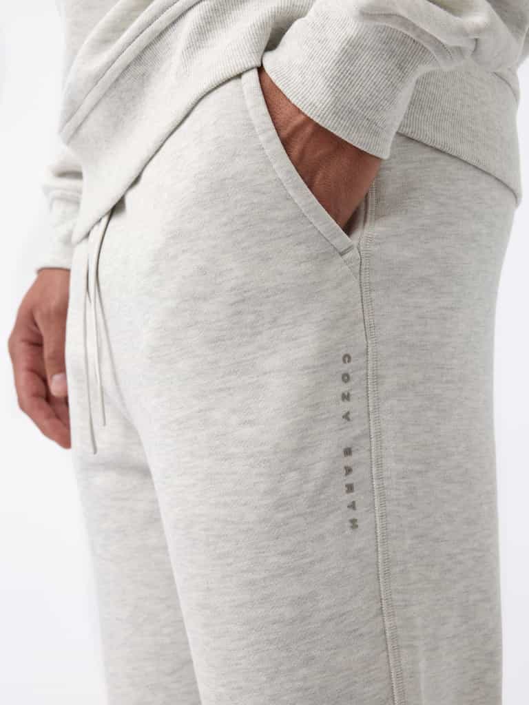A person wearing Cozy Earth's Men's CityScape Jogger in light gray with their hand in the pocket. The joggers feature a subtle logo or text running vertically down the side and the fabric appears soft and comfortable. |Color:Heather Grey