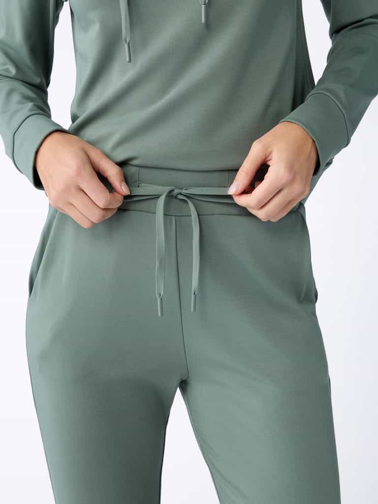 A person wearing the Women's Bamboo Jogger Pant TALL in green from Cozy Earth adjusts the drawstring on the pants. The image is focused on the torso and hands, highlighting the comfortable, casual outfit. |Color:Oakmoss