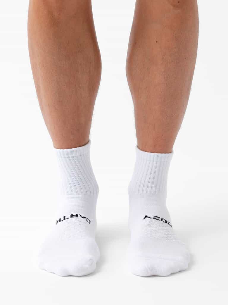 A person wearing Cozy Earth's Essential Quarter Sock 6-Pack stands on a white surface, showing only their lower legs and feet. |Color:White