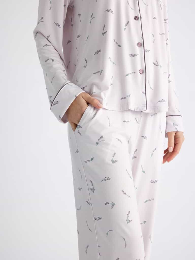 A person wears Cozy Earth Women's Bamboo Stretch-Knit Pajama Pants featuring a subtle branch pattern and matching pajama top with dark piping and buttons, with one hand in the pants pocket. The background is plain white. |Color:French Lavender