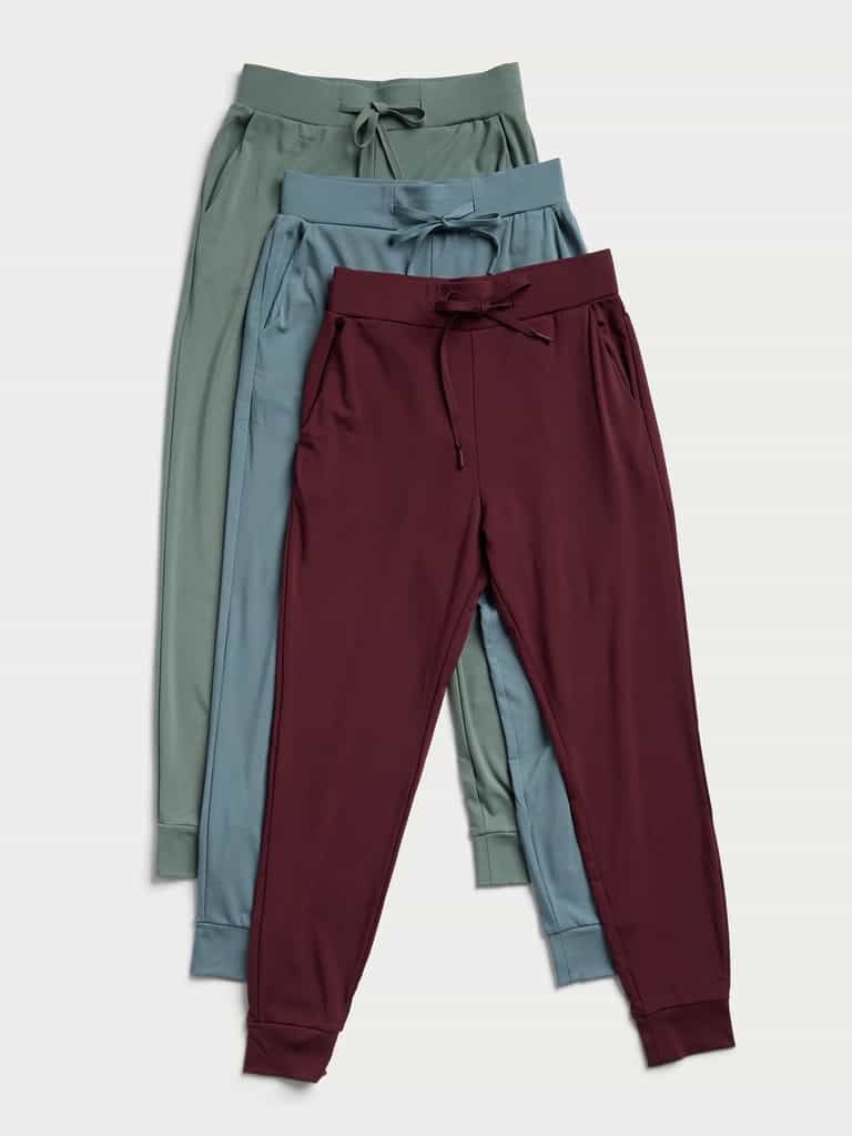 Three pairs of the Women's Bamboo Jogger Pant by Cozy Earth, in green, blue, and maroon, are placed overlapping each other. Each pair showcases a drawstring waist and cuffed ankles against a light background. |Color:Oceanside