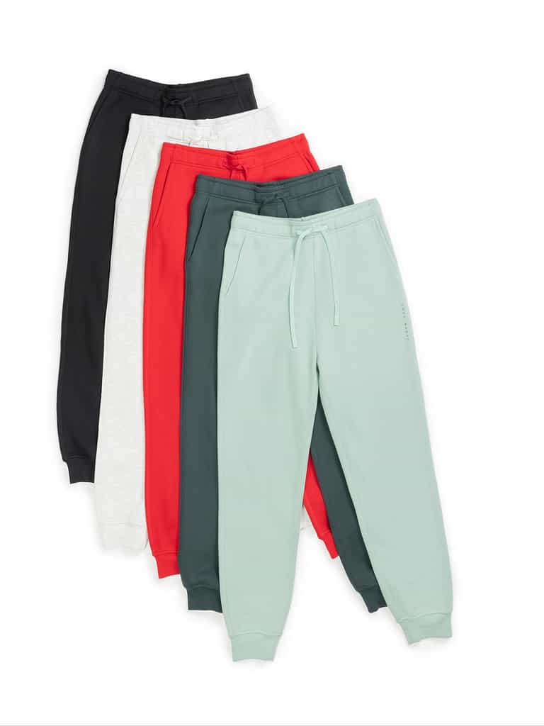 A set of five pairs of Men's CityScape Joggers by Cozy Earth arranged in a fan shape, available in black, gray, red, green, and light teal. Each pair features a drawstring waist and cuffed ankles. |Color:Spruce
