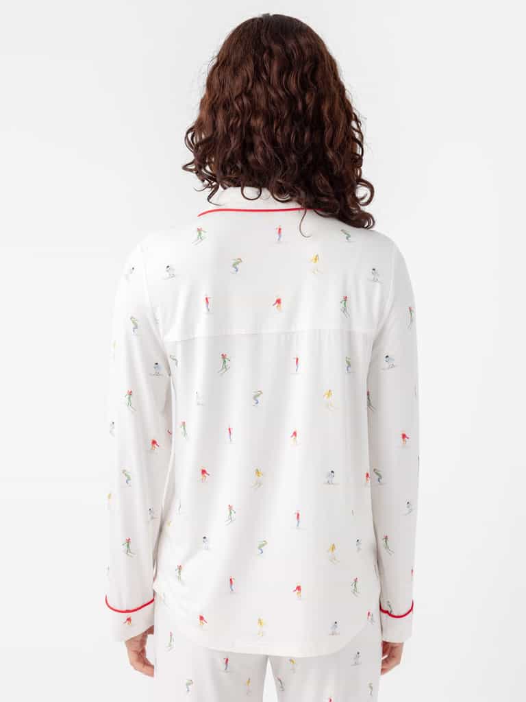 Rear view of a person with long, curly hair wearing Cozy Earth's Last Chance Women's Bamboo Stretch-Knit Long Sleeve Pajama Set. The sleepwear features colorful skier prints and red piping on the collar and cuffs against a plain white background. |Color:Skiers Ivory