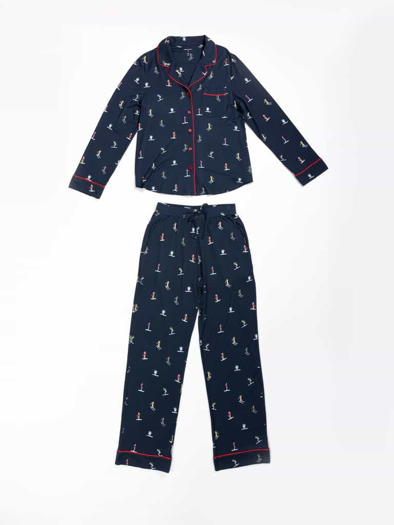 The Last Chance Women's Bamboo Stretch-Knit Pajama Set by Cozy Earth is navy blue with small multicolored ski prints, features a collared, button-down long-sleeve top with red piping, and drawstring waist pants. |Color:Skiers Navy