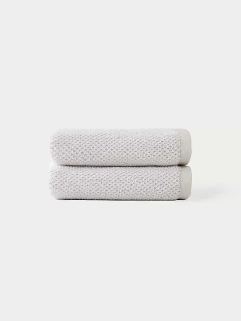 Two Nantucket Bath Towels by Cozy Earth, in light gray, are neatly folded and stacked against a plain white background.|Color:Heathered Light Grey