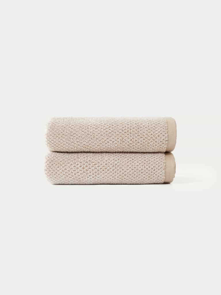 Two Nantucket Bath Towels by Cozy Earth, neatly folded and stacked atop each other, are displayed against a plain white background.|Color:Heathered Sand