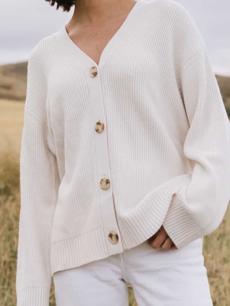 A woman wearing Cozy Earth Classic Cardigan in white stands in a field. She is pictured from the neck down |Color:Ivory