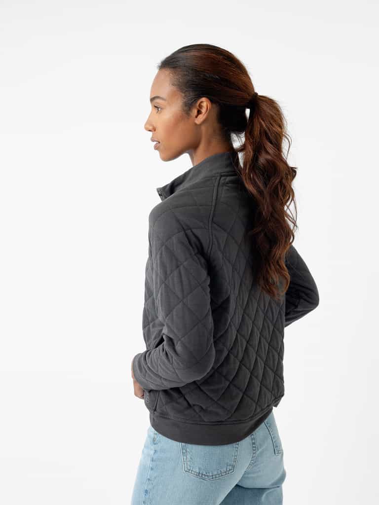 A person with long hair styled in a ponytail is turned to the side, dressed in Cozy Earth's Women's Ultra-Soft Bamboo Quilted Snap Pullover and light blue jeans. The background is white and minimalistic. |Color:Charcoal
